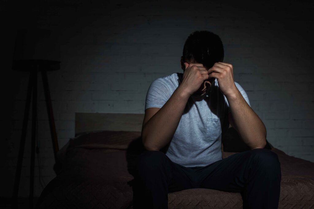 a stressed man with head in hands sat on bed