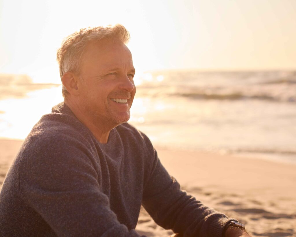 retired man sat on beach smiling